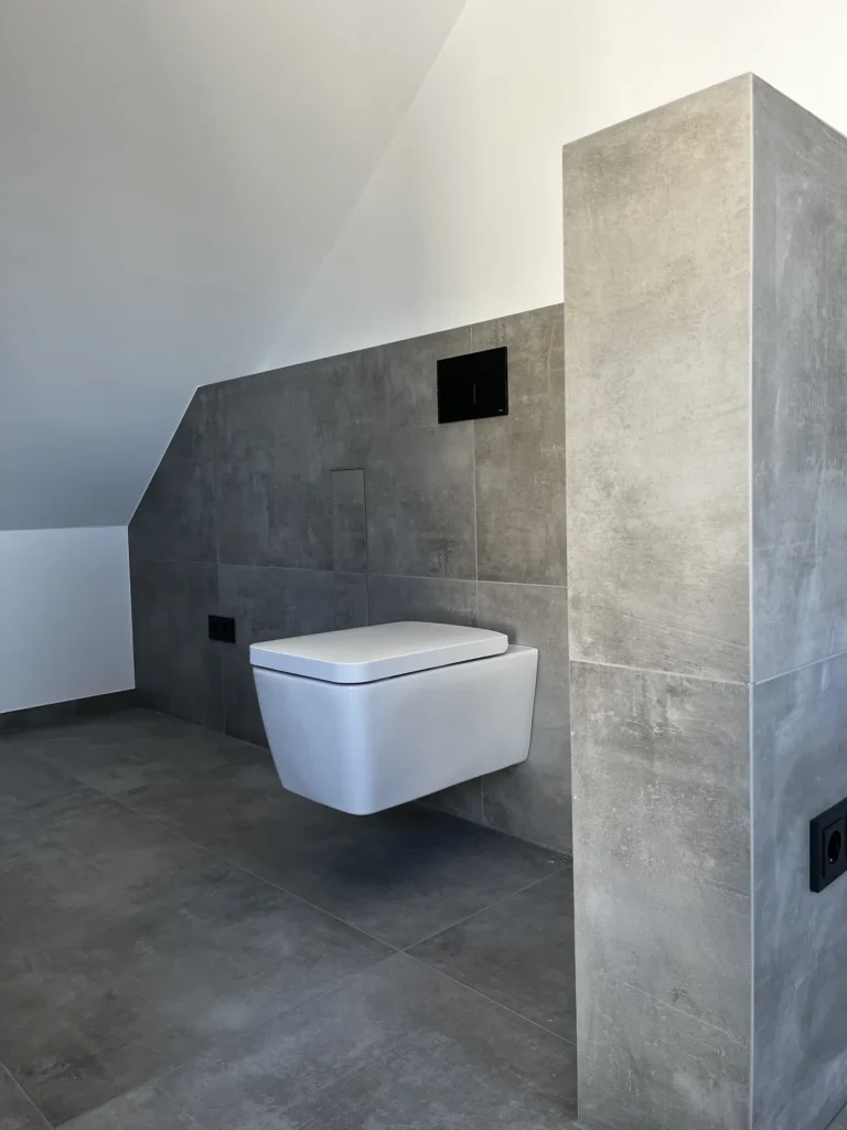 Bad unter der Dachschräge mit WC-Vorwand aus grauen Fliesen in Betonoptik